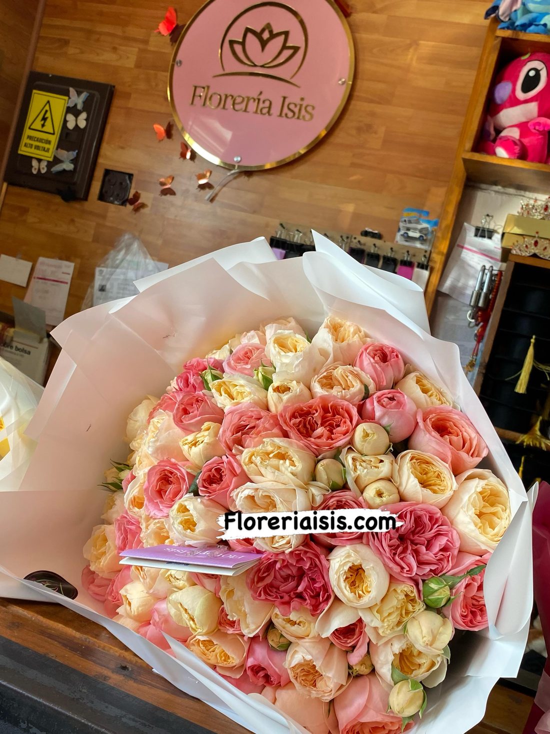 Ramo de rosas inglesas en tonos durazno y rosa sobre el mostrador de Florería Isis, con el letrero del loto al fondo